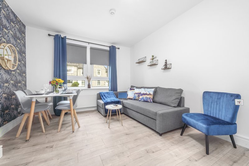 Modern living room with gray sofa, blue armchair, dining table and window with blue curtains