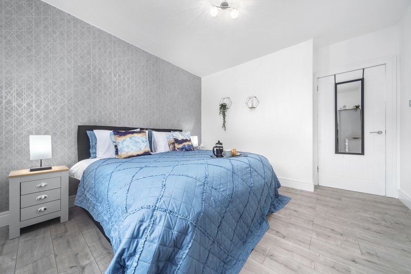 Modern bedroom with blue bedding, grey headboard, wooden floor and ensuite door