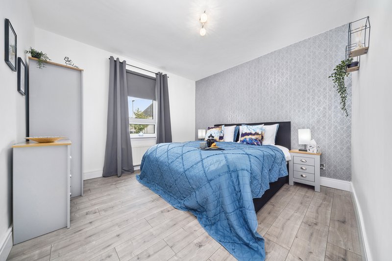 Modern bedroom with double bed, blue quilt, bedside tables, and patterned accent wall