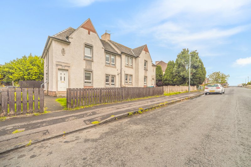 Cream-coloured stone house with wooden fence, driveway, and surrounding gardens