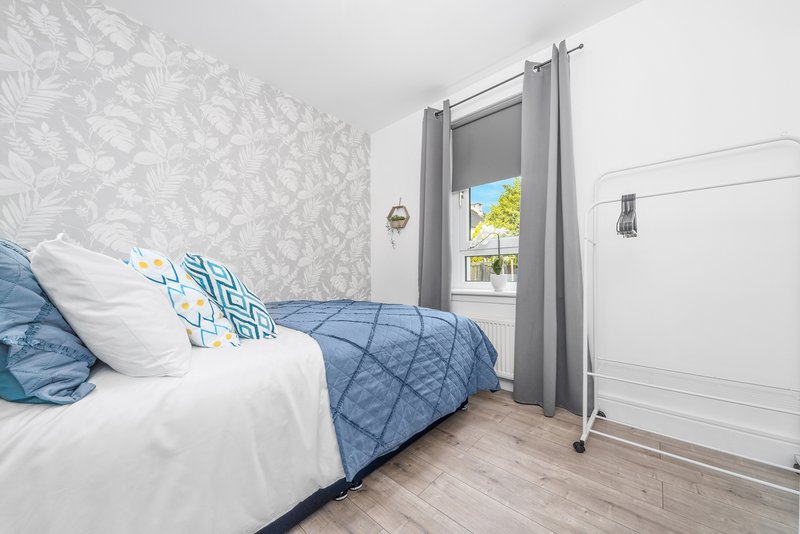 Bright bedroom with double bed, blue bedding, patterned wallpaper and wooden floor