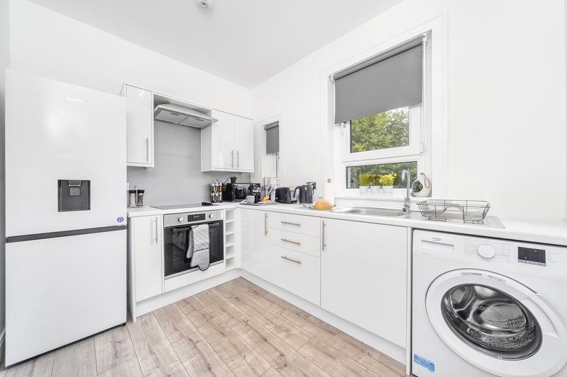 Modern white kitchen with integrated appliances, washing machine, and wooden flooring