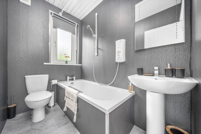 Modern bathroom with bathtub, pedestal sink, toilet, and window with natural light