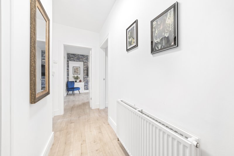 Bright hallway with wooden flooring, white walls, framed artwork, and radiator