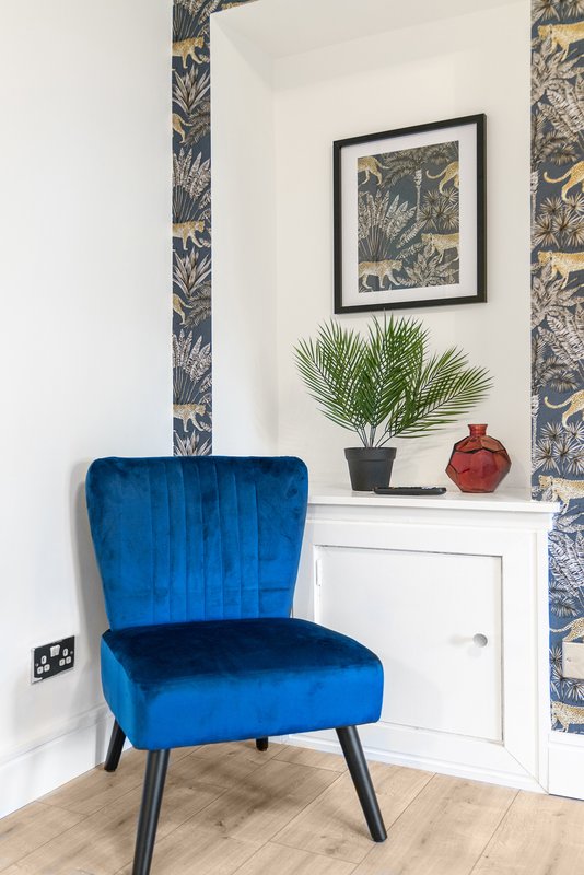 Blue velvet accent chair in corner with white cabinet, framed botanical art and potted plant