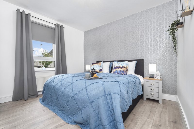 Modern bedroom with double bed, blue quilt, grey curtains and patterned wallpaper