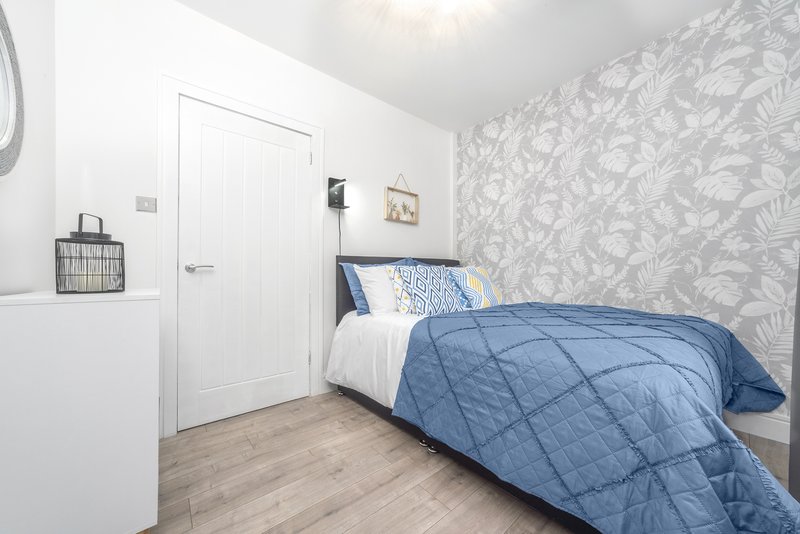 Bedroom with single bed, blue bedding, patterned wallpaper, wooden floor and white door