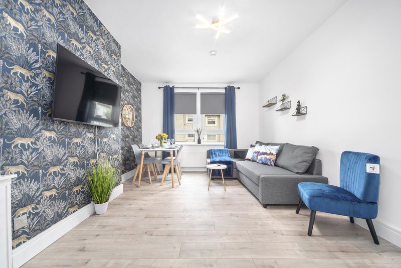 Modern living room with patterned accent wall, sofa, blue armchair, dining table and wall-mounted TV