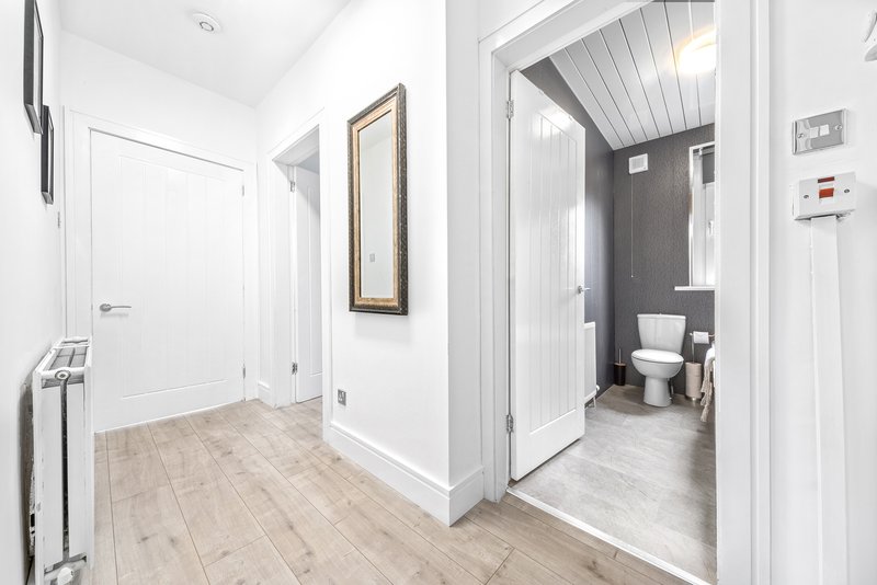Modern hallway with light wood flooring, white walls, framed mirror and open bathroom door