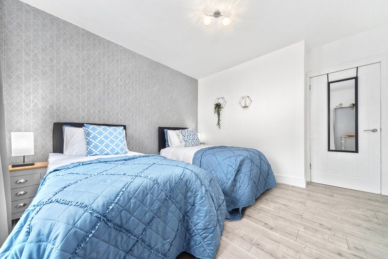Bright bedroom with two single beds, blue quilts, patterned wallpaper and wooden flooring