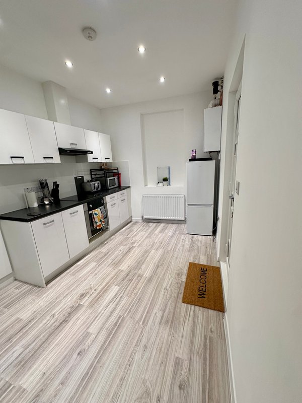 Modern kitchen with white cabinets, black countertops, stainless steel appliances and wooden flooring.
