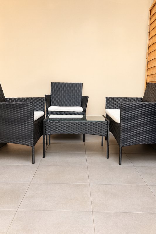 Outdoor patio area with three black wicker chairs and small table on tiled floor