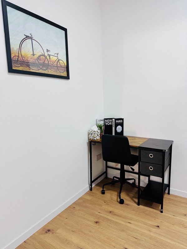 Compact workspace with black desk, office chair, and framed fairground print on white wall