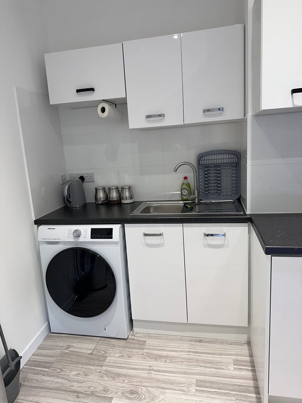 Compact kitchenette with white cabinetry, washing machine, sink and stove area