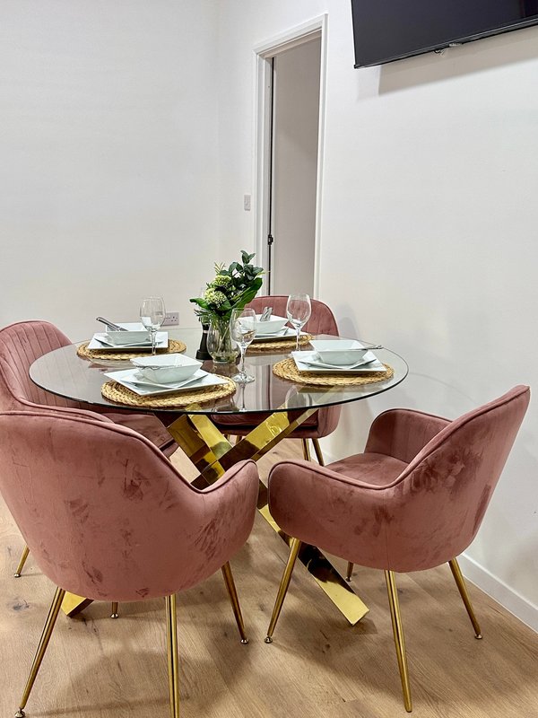 Dining area with round glass table, four pink velvet chairs, place settings, and fresh flowers
