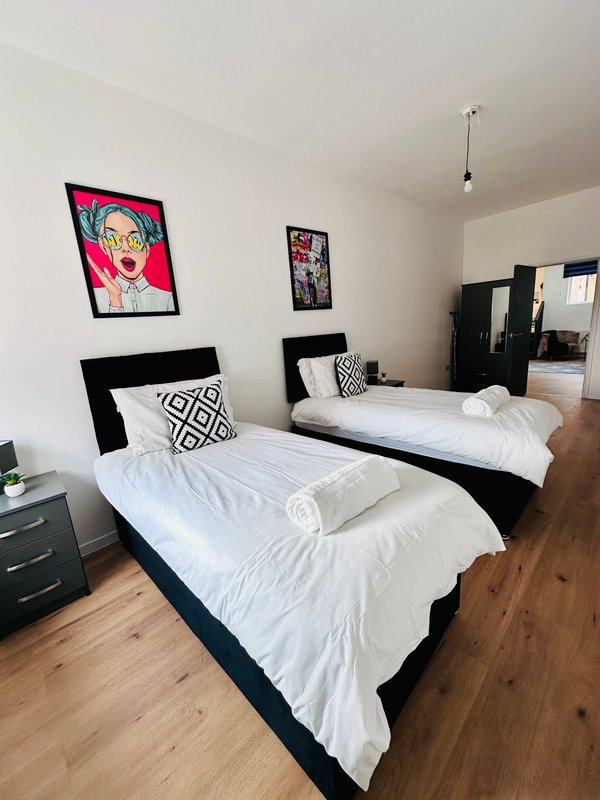 Modern bedroom with two black beds, white bedding, wooden floor and framed wall art