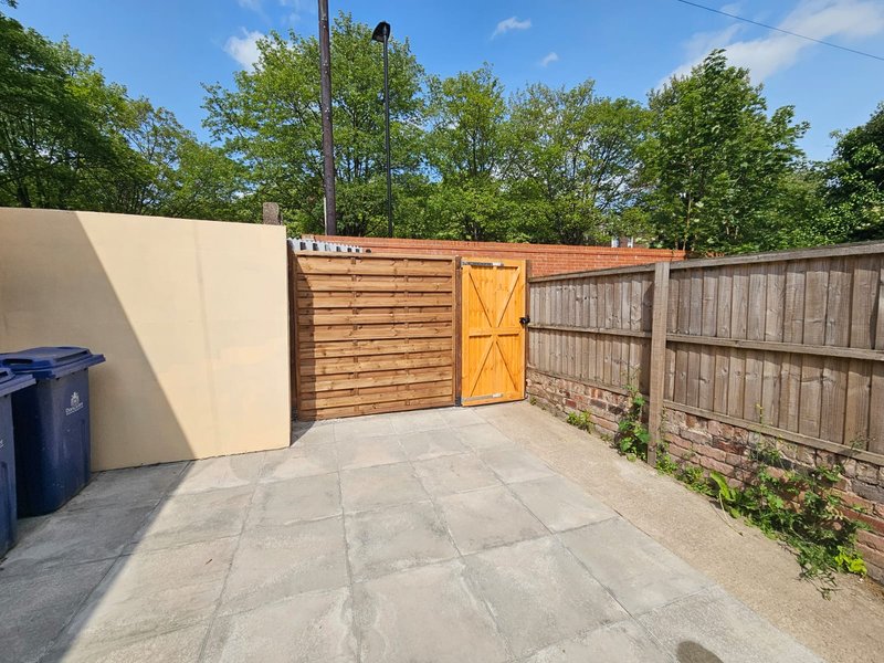 Outdoor paved area with wooden gates, fencing and recycling bin