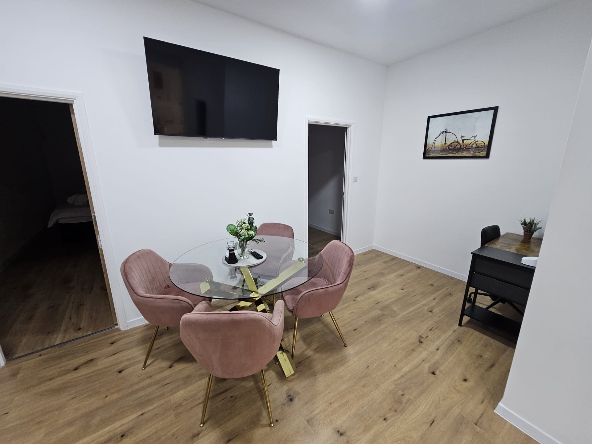 Modern living room with round glass table, pink velvet chairs, wall-mounted TV and wooden flooring