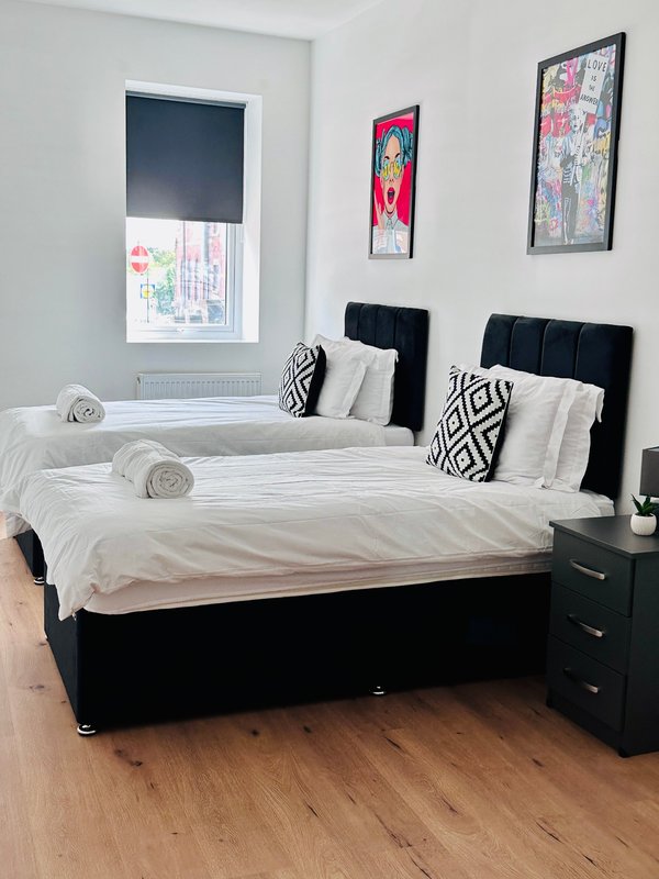 Bright bedroom with two black beds, white bedding, patterned cushions and wall art