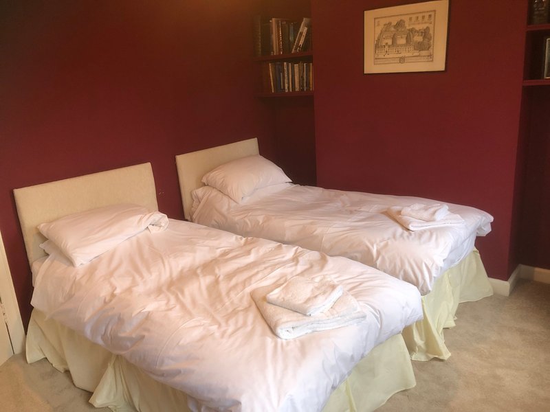 Bedroom with two single beds, cream bedding, burgundy walls, and wall shelving with books