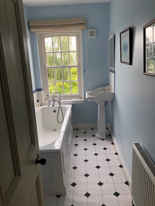 Bathroom with bathtub, pedestal sink, window overlooking garden, black and white tile floor