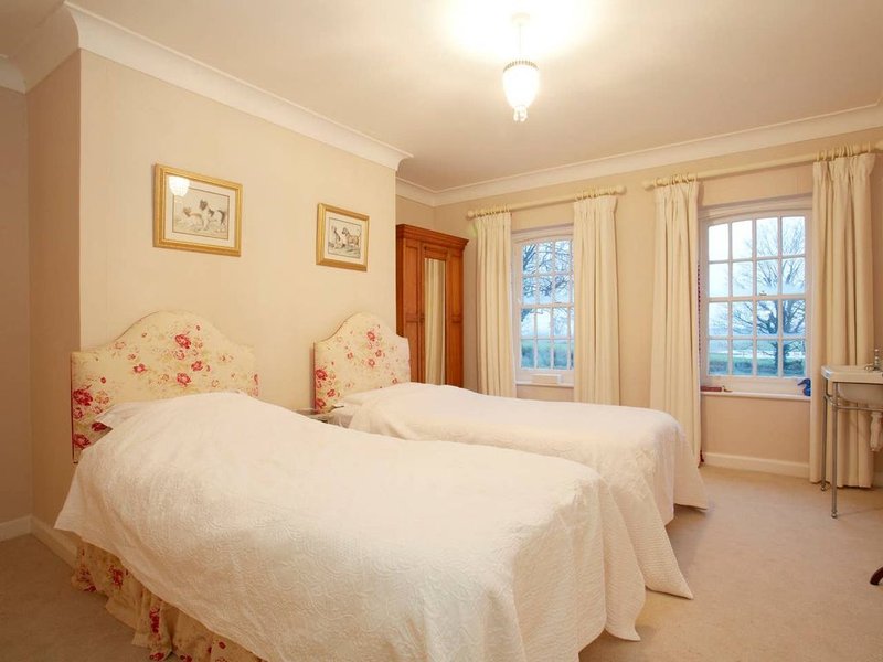 Twin bedroom with floral headboards, white bedding, framed artwork, and bay windows with cream curtains