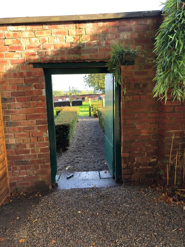 Brick passageway with open doorway leading to garden with green lawn and hedges
