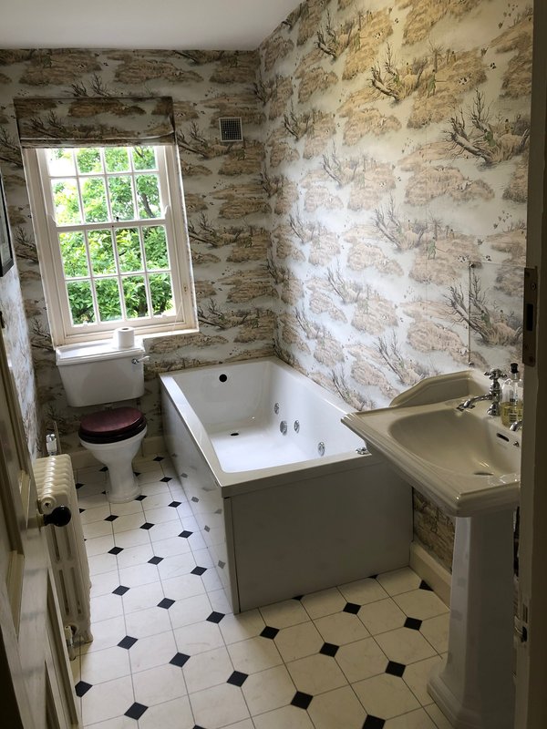 Bathroom with bathtub, toilet, sink, patterned wallpaper and window