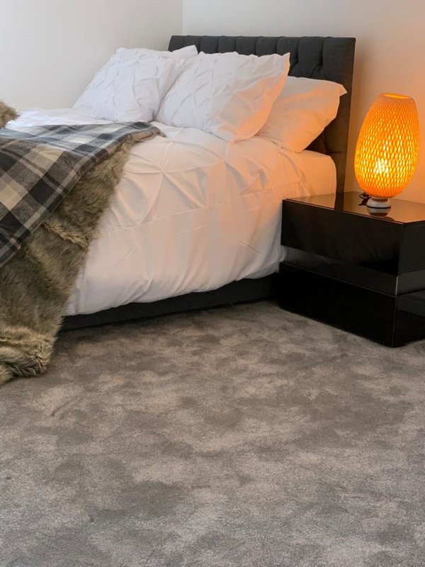Modern bedroom with black bed frame, white pillows, orange bedding, plaid throw, and orange bedside lamp