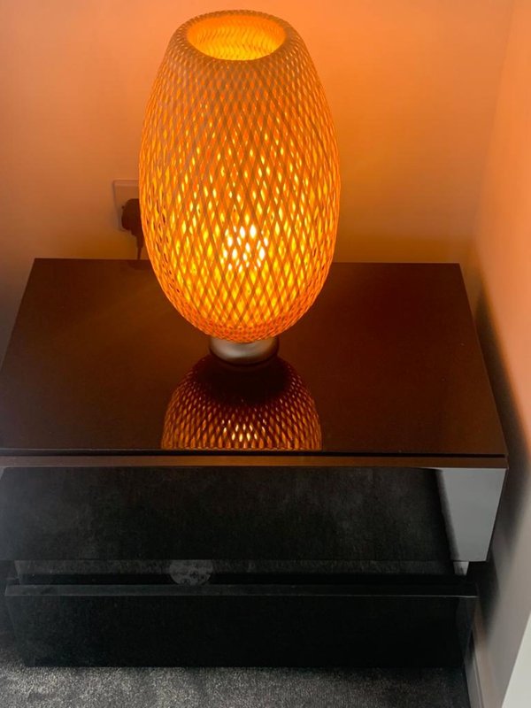 Orange woven pendant lamp with warm glow on black bedside table