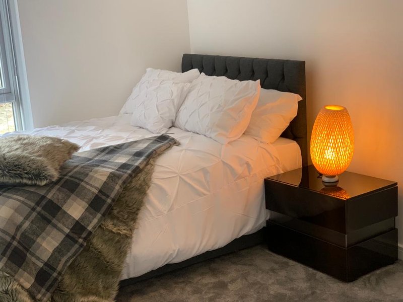 Bedroom with double bed, black headboard, white bedding, plaid throw blanket, and orange bedside lamp