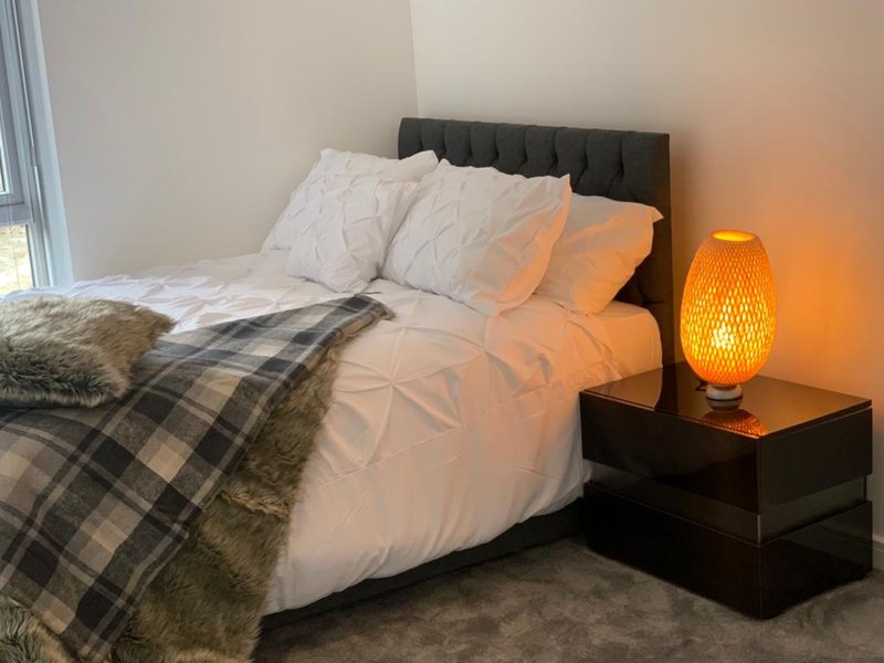 Bedroom with double bed, black headboard, plaid throw blanket, and orange bedside lamp