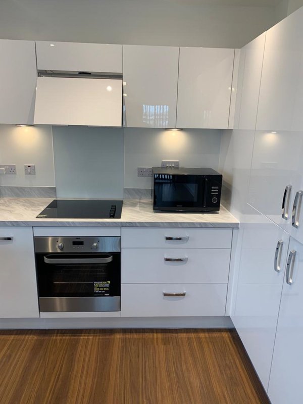 Modern white kitchen with built-in oven, microwave, wooden flooring and overhead cabinets