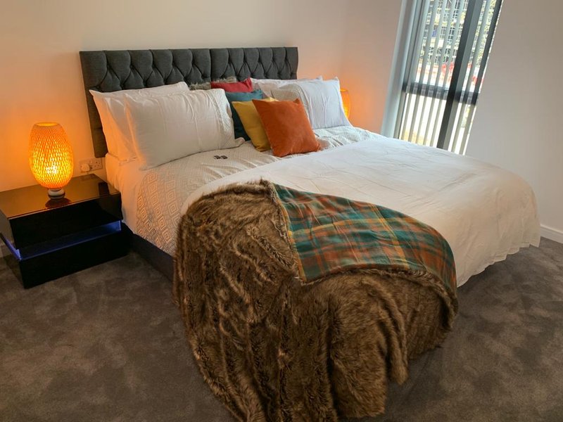 Modern bedroom with grey upholstered headboard, white bedding, decorative pillows and throws