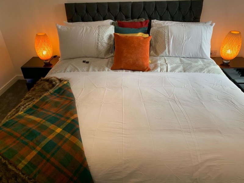 Modern bedroom with upholstered headboard, white bedding, decorative pillows, and orange accent lamps