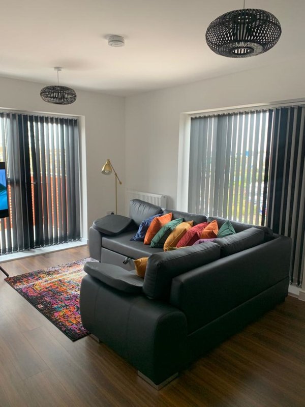 Modern living room with black leather sofa, colorful cushions, floor lamp, and vertical blinds