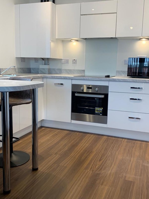 Modern white kitchen with built-in oven, breakfast bar, and wooden flooring