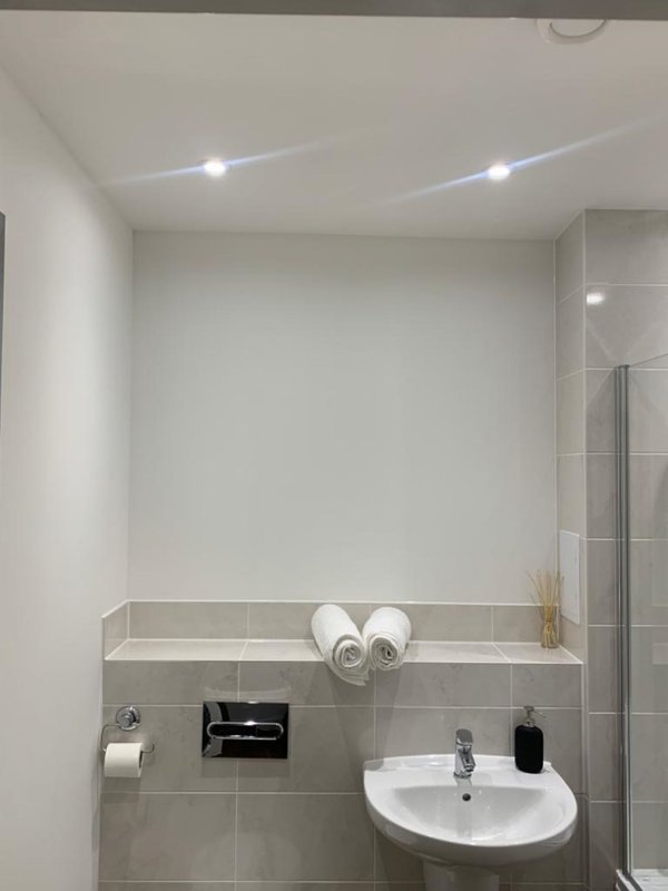 Modern bathroom with white sink, grey tile walls, towel rail and recessed lighting