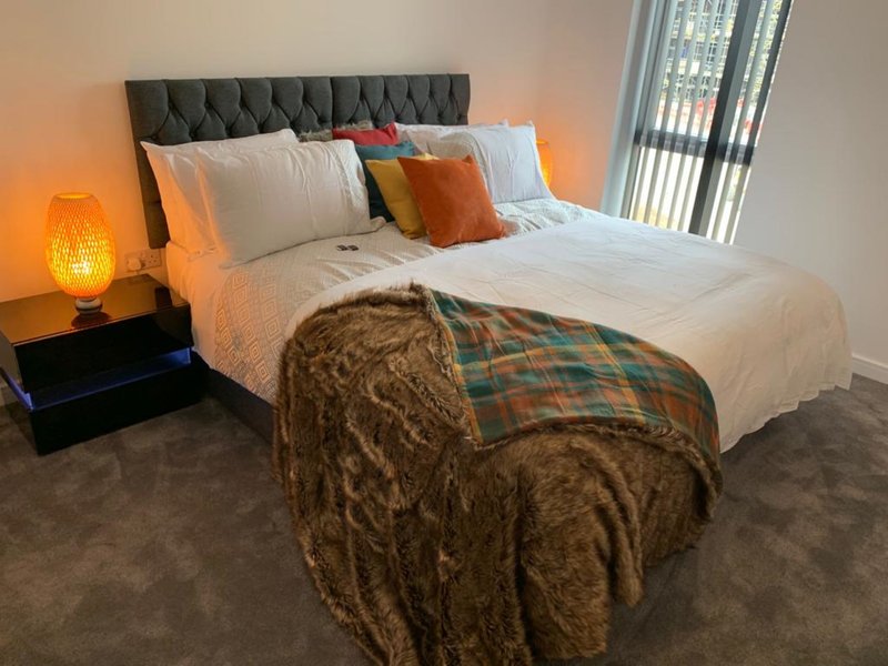 Modern bedroom with grey upholstered headboard, white bedding, plaid throw, and bedside lamp