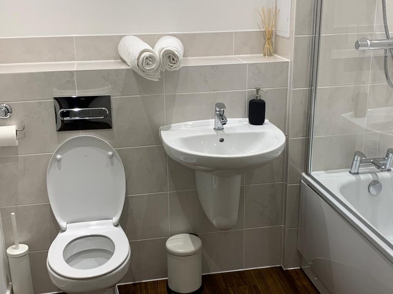 Modern bathroom with toilet, pedestal sink, shower enclosure and grey tile walls