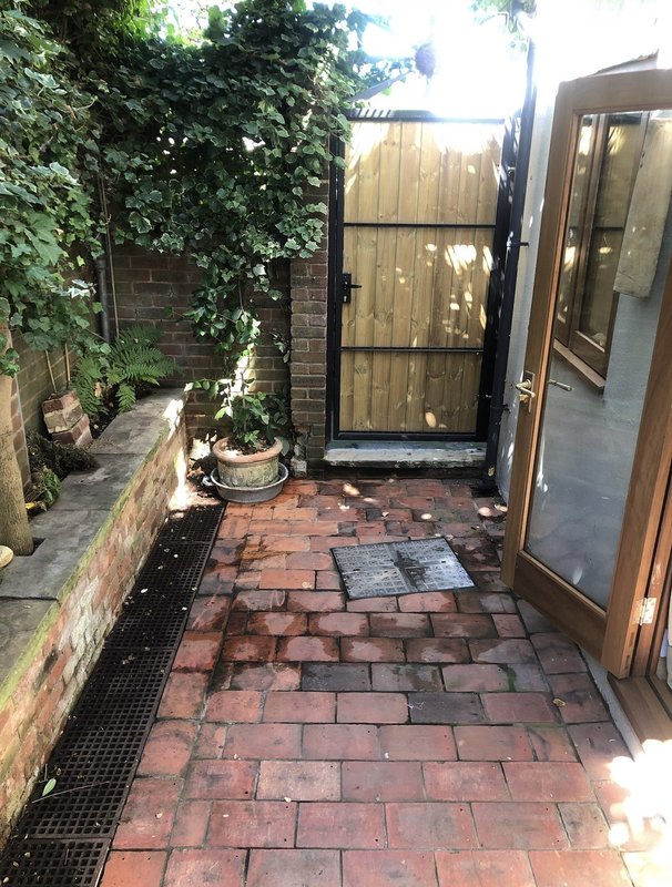 Brick paved outdoor courtyard with wooden gate, climbing ivy, and potted plants