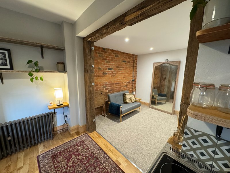 Open-plan living area with exposed brick wall, wooden beams, radiator and seating area