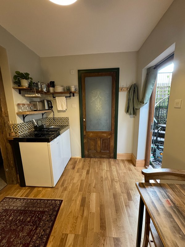 Kitchenette with white cabinetry, wooden flooring, shelving, and door to bathroom