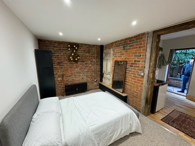 Bedroom with double bed, exposed brick walls, wooden beams and recessed ceiling lights