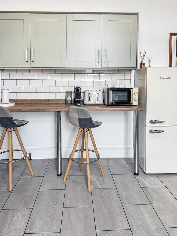 Modern kitchen with white cabinetry, subway tile backsplash, wooden countertop, bar stools and retro refrigerator