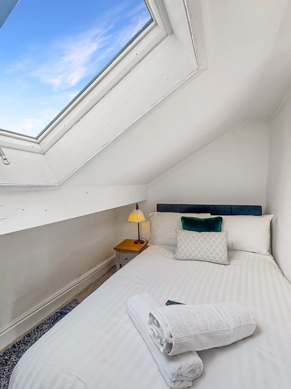 Bright attic bedroom with skylight, single bed, wooden nightstand and yellow lamp
