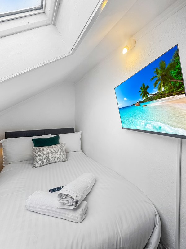 Compact bedroom with single bed, skylight window, cushions and wall-mounted TV screen