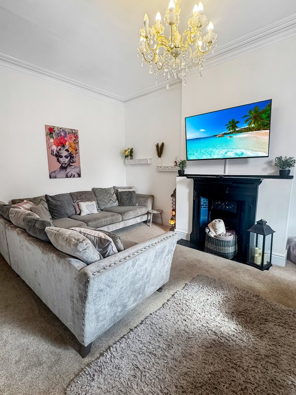 Spacious living room with grey upholstered sofa, fireplace, TV, crystal chandelier and artwork