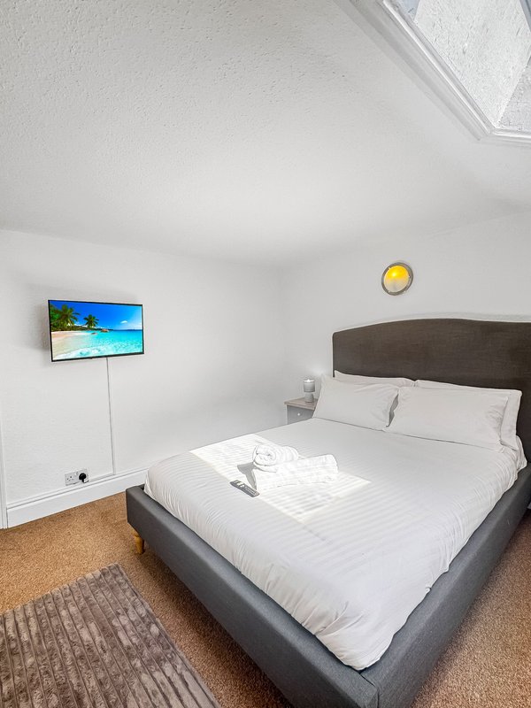 Bedroom with double bed, wall-mounted TV, yellow clock and white bedding