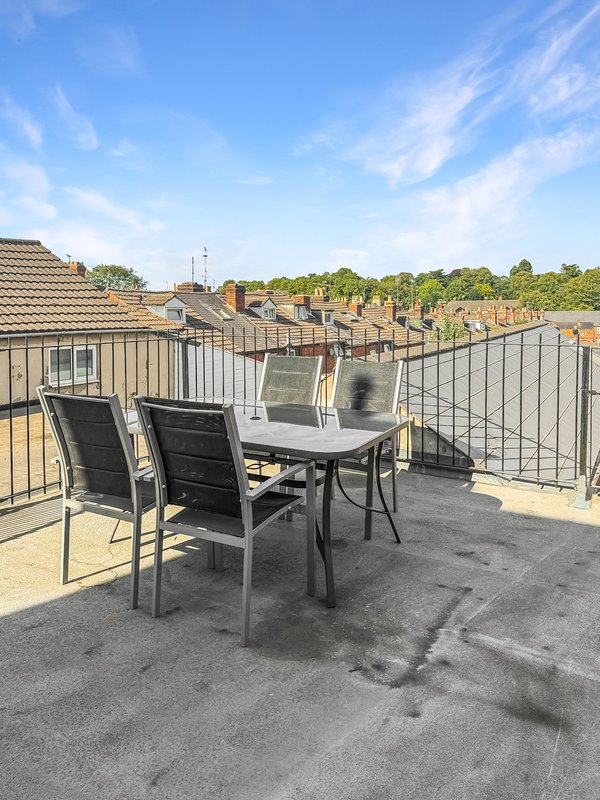 Rooftop terrace with dining table, chairs, and metal railing overlooking residential area